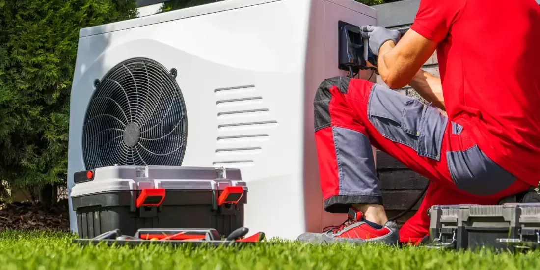 A heating technician in red working on an outdoor heat pump unit