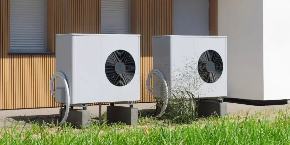 Two light grey heat pumps side by side in front of a property