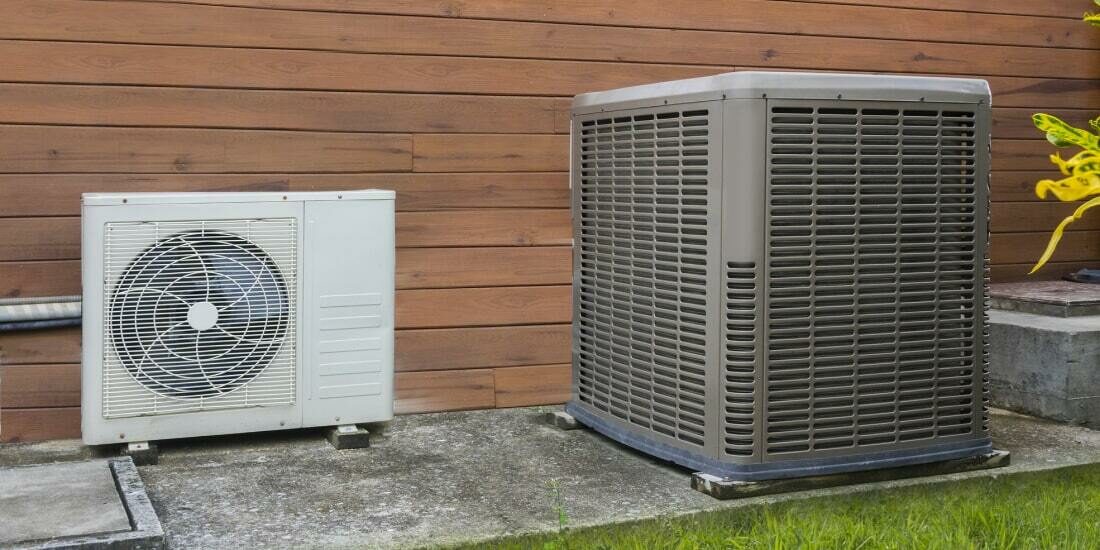 Two different sized air conditioning heat pumps on side of house.