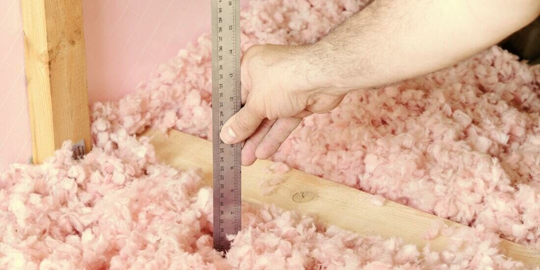 A person placing a metal ruler into blown insulation