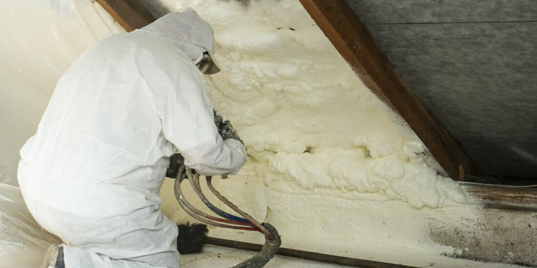 Installer spraying foam insulation in loft