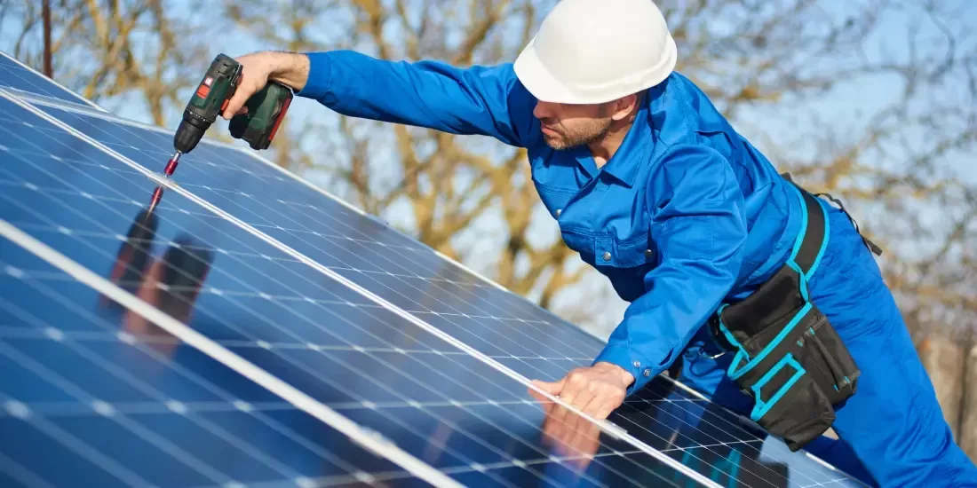 Solar panel installer in a blue boiler suit fixing a panel to the roof of a house
