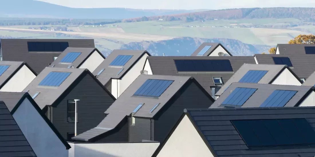New build properties with solar panels on their roof against a backdrop of Scottish hills