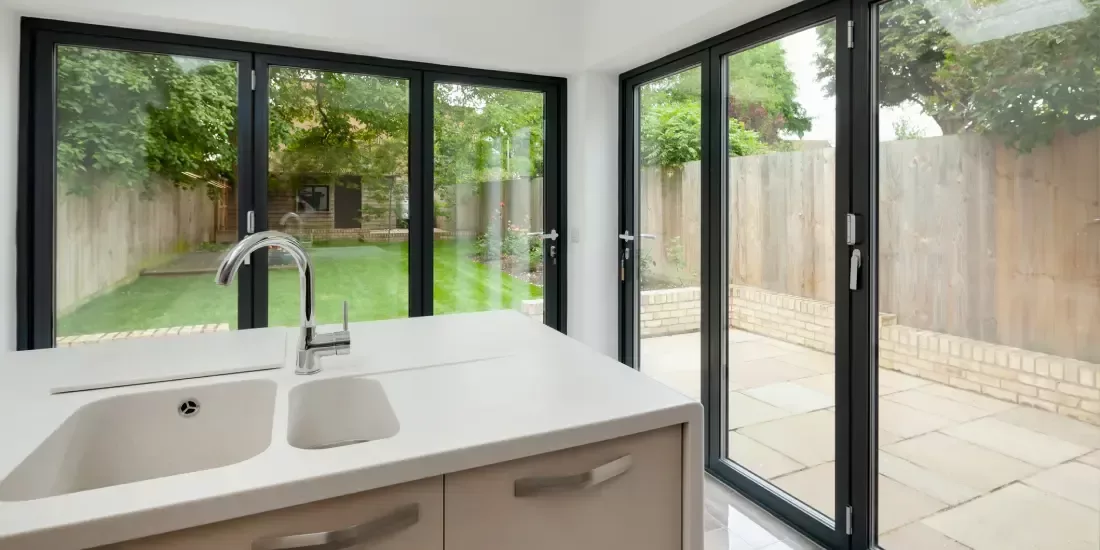 A modern kitchen with aluminium bifold doors and windows overlooking a garden