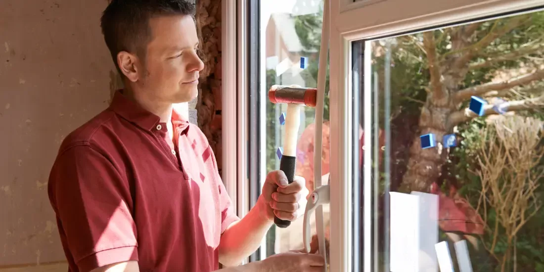 A window installer in red hammers in the seal around a new window installation
