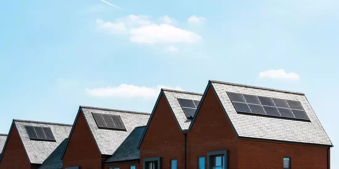 A row of several houses with solar panels on their roofs against a blue sky backdrop