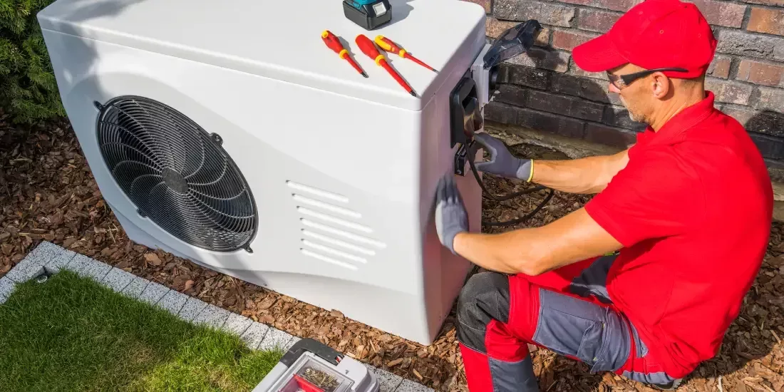 A heating technician in a red polo shirt altering the control panel of an outdoor heat pump unit