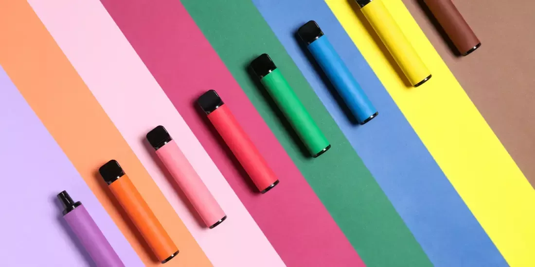 Coloured disposable vapes against a coloured striped background
