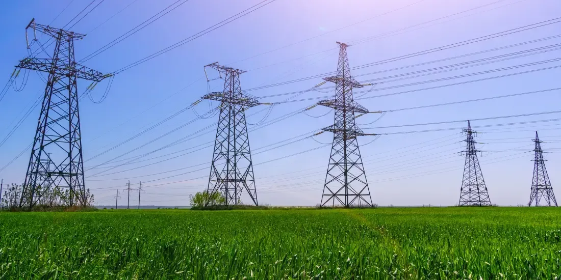 Electricity pylons in a grassy field against a blue sky