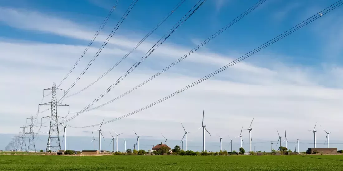 Electricity pylons in a field with a wind farm alongside