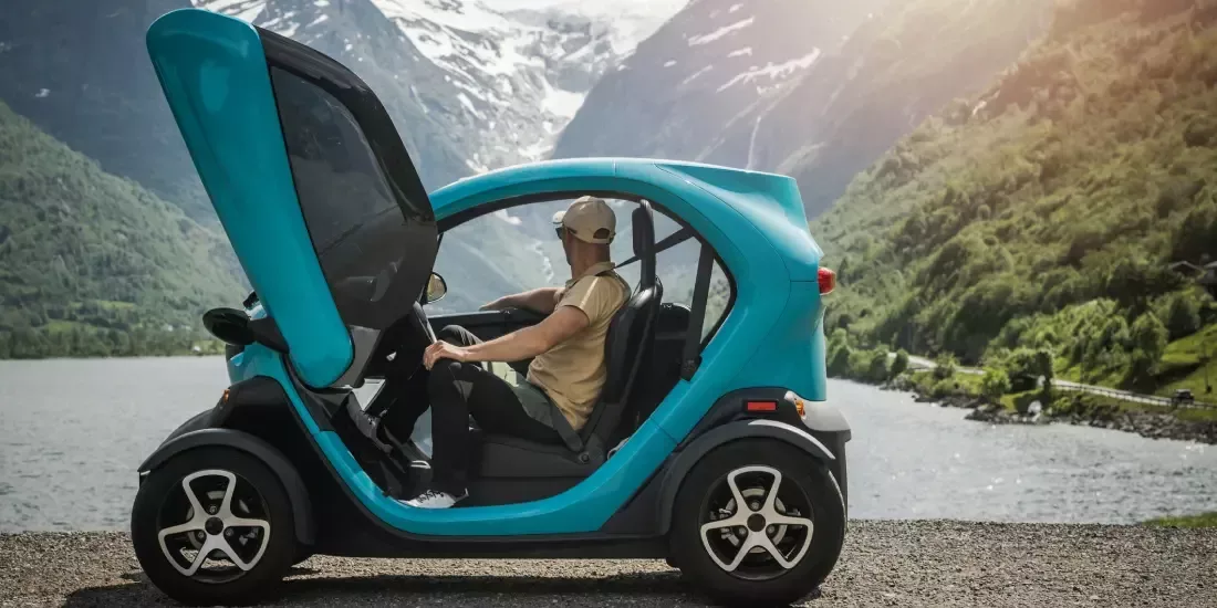 A tourist looking at the mountains of Norway from the seat of a small electric vehicle parked beside a lake