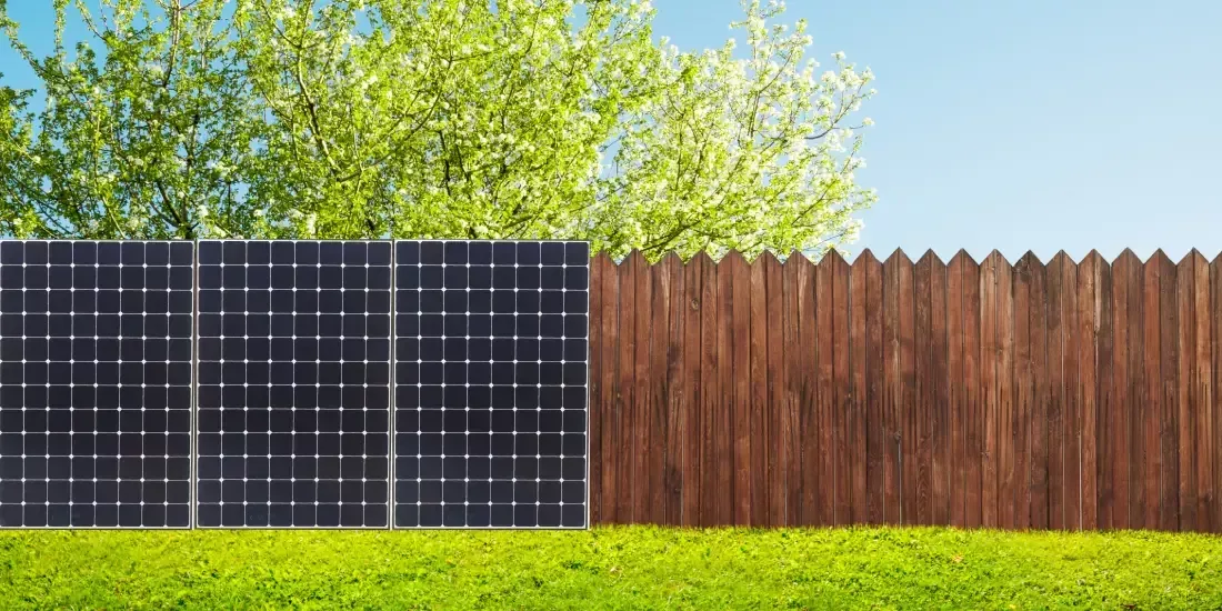 A wooden fence across a garden with half of it replaced by solar panels